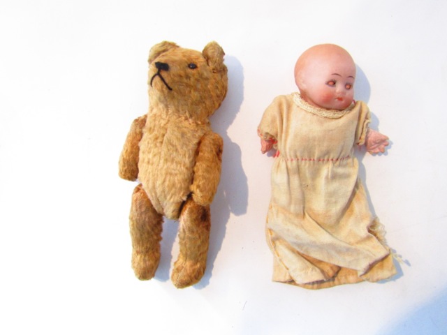 A small bisque head doll and a vintage straw filled teddy with bead eyes