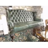 A Georgian style three seat sofa, green leather upholstered, rolled arms, winged and buttoned back