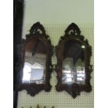 A pair of continental wall mirrors set within carved timber frames of oval form with scrolling,