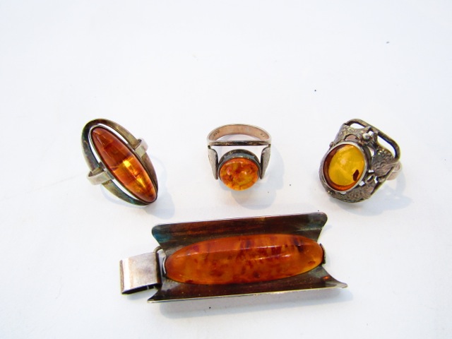 An amberoid ring, with stylised fish border, in silver; two further amberoid rings, in silver; and