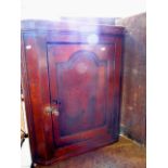 A small Georgian oak hanging corner cupboard enclosed by a fielded arched panelled door, the