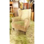 A late Victorian/Edwardian wing armchair with shaped outline, upholstered finish and turned forelegs