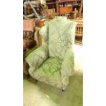 An Edwardian wing armchair in the Georgian style with shaped outline, floral patterned upholstery on