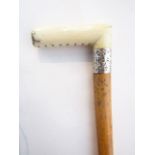 An antique Malacca walking cane terminating in a worked ivory handle set above an embossed silver