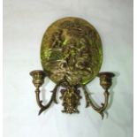 A brass two divisional wall sconce, the oval shaped backing plate embossed with a scene depicting