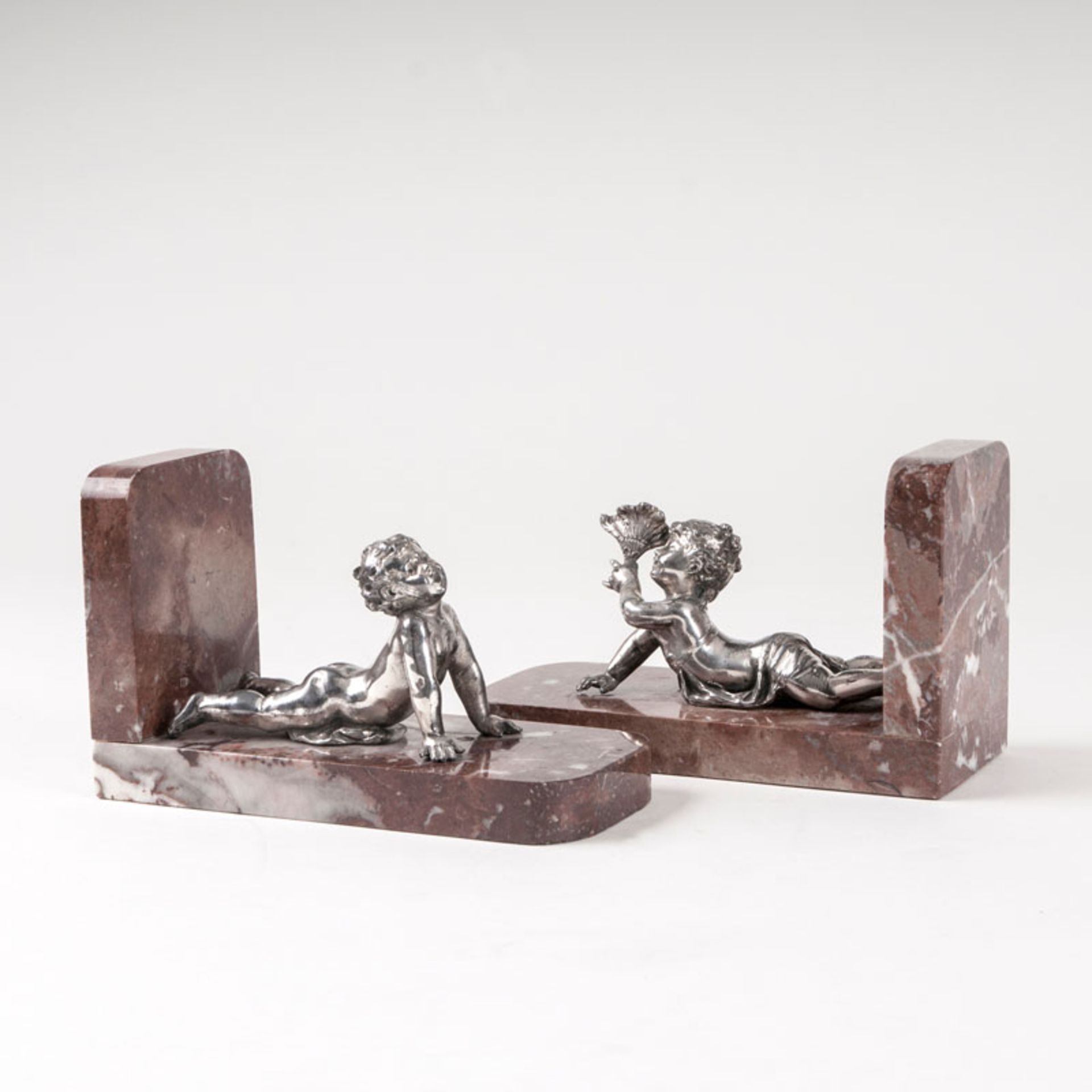 A pair of decorative bookends with putti Around 1900. Metal, silver-plated. Reclining putto on a