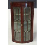 A GEORGE III MAHOGANY BOWFRONTED CORNER CABINET the outswept pediment above a plain frieze, a pair