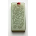 A CHINESE CELADON JADE-LIKE STONE PENDANT rectangular, carved with a dragon amongst clouds, the