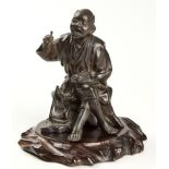 A JAPANESE PATINATED BRONZE OKIMONO OF A FARMER, MEIJI, 1868-1912 seated on a tree stump and