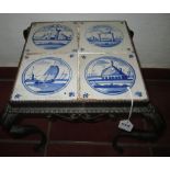 A DUTCH DELFT BLUE AND WHITE TILE AND CAST IRON LOW TABLE with four tiles painted with landscape