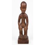 A CARVED MALE FIGURE, POSSIBLY MADAGASCAR the standing figure with his hands on his knees, inscribed