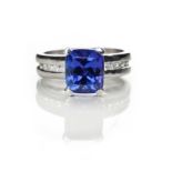 A TANZANITE AND DIAMOND RING claw set to the centre with a cushion-cut diamond weighing 3.84cts, the