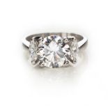 A DIAMOND RING centred with a claw-set brilliant-cut diamond weighing 3.008cts, flanked on either