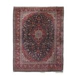 A KESHAN CARPET, PERSIA, MODERN the dark indigo field with a red and ivory floral medallion, similar