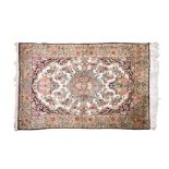 A QUM SILK RUG, PERSIA, MODERN the ivory field with a rose floral medallion, dark-blue spandrels all