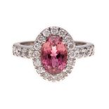 A PINK TOURMALINE AND DIAMOND RING of halo design, centred with an oval mixed-cut pink tourmaline