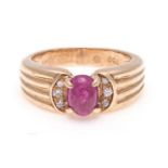 A RUBY RING the tapered fluted band centred with an oval cabochon ruby, flanked on either side by