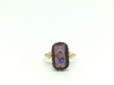 Unusual yellow metal ring set with a purple stone panel which is painted with a lady carrying a