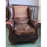 A leather wingback armchair with upholstered back and sides, raised on bun feet.
