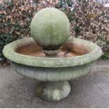 An antique stone fountain, the central sphere within an urn raised on a pedestal base.