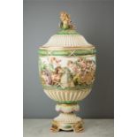 An Italian Capodimonte urn and cover profusely decorated with relief modelled cherubs, chariots,