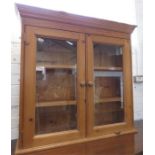 A pine bookcase with glazed doors enclosing two sh