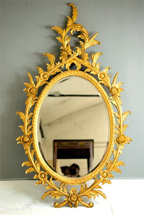 A giltwood oval wall mirror, carved with Rococo style scrollwork.