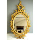 A giltwood oval wall mirror, carved with Rococo style scrollwork.