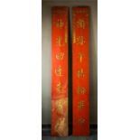 A pair of Chinese painted panels, with carved and gilded calligraphy on a red ground.