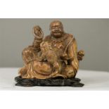 A 19th century Chinese soapstone Buddha, holding disc, peach and frog, raised on an ebonised