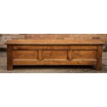 An 18th century oak settle base with a two plank lid, the front with three fielded panels, raised on