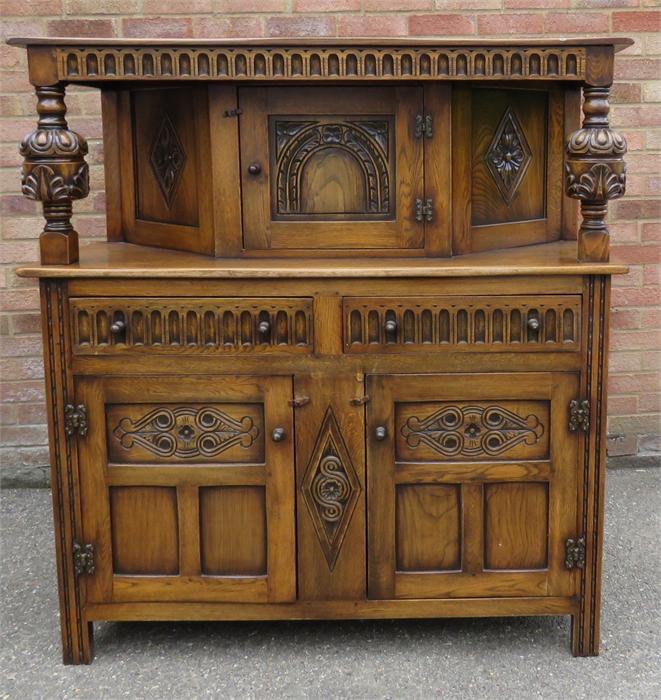 A reproduction oak court cupboard with baluster supports and canted top section.