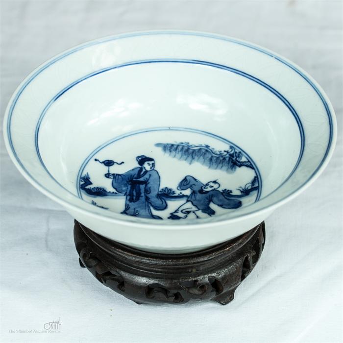A 19th century Chinese blue and white bowl on carved wooden stand, with calligraphy to the base.