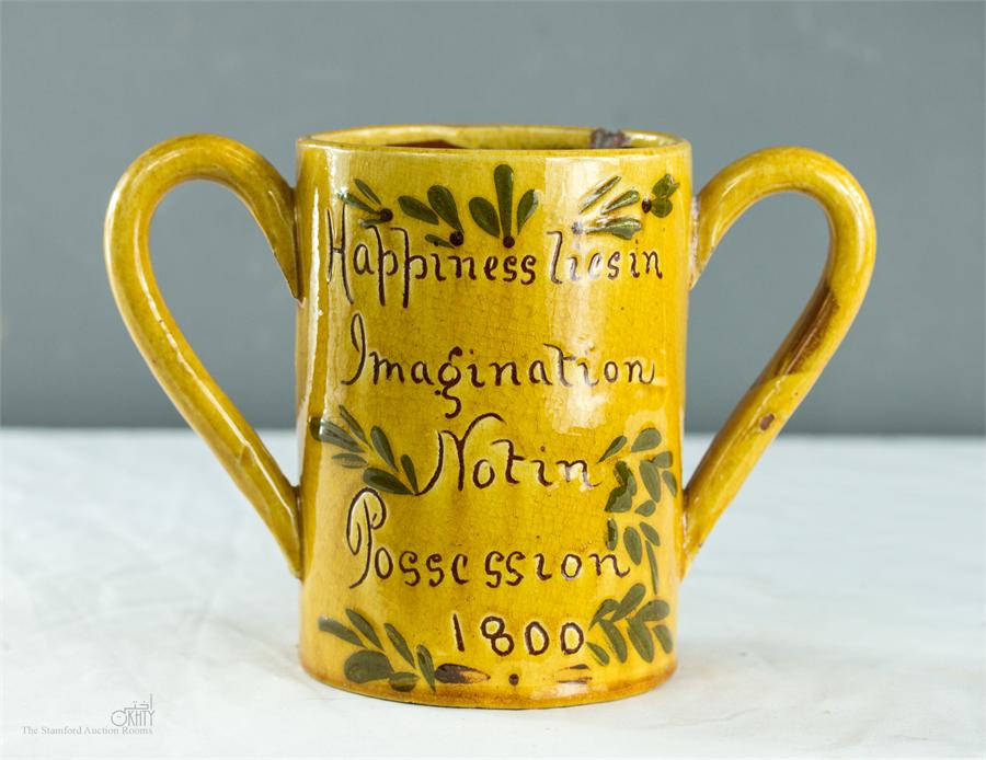 An early 19th century slipware twin handled mug, 'Happiness Lies in Imagination Not in Possession,