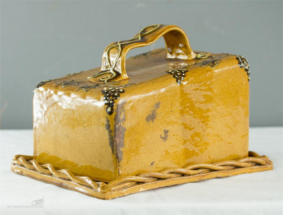 A treacle glazed stoneware cheese dish, possibly 19th century, with grape and vine slip design.