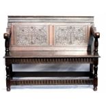 An oak settle, the back carved with stylised foliage, the shaped arms raised on turned supports,