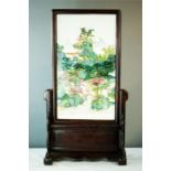 A Chinese porcelain plaque painted with figures in a mountainous landscape, mounted in a carved