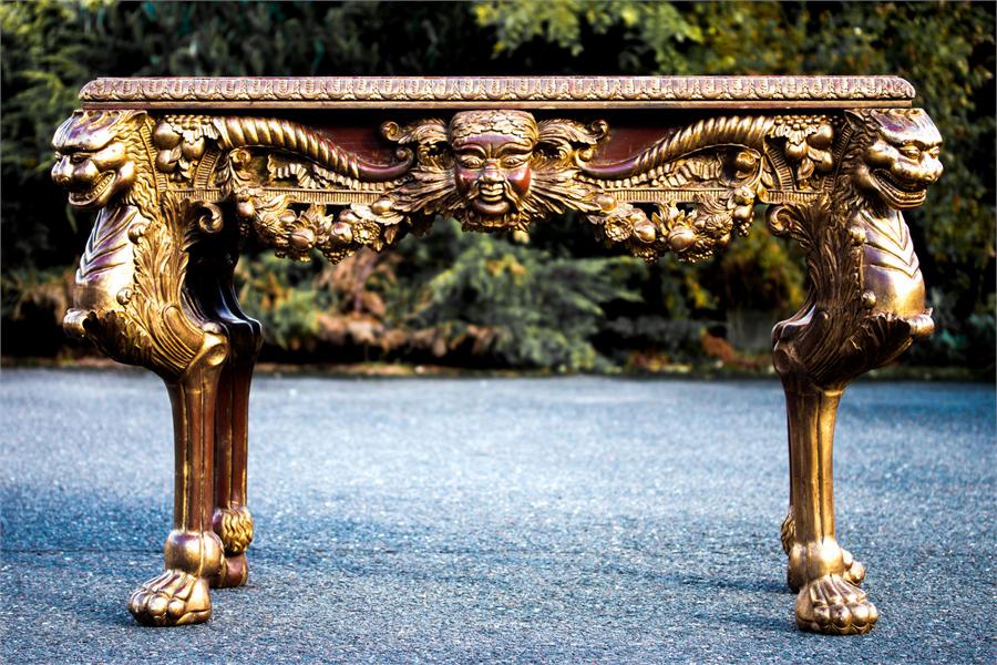 A Baroque style giltwood console table, carved with faces masks, swags and foliage. 84cm high, 131