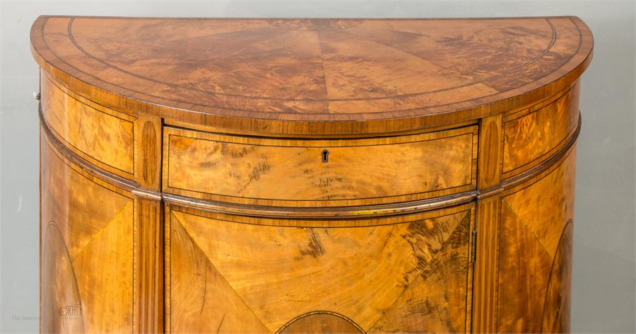 A 19th century demi-lune satinwood and mahogany commode with oval veneered sides and door, raised on - Image 2 of 2