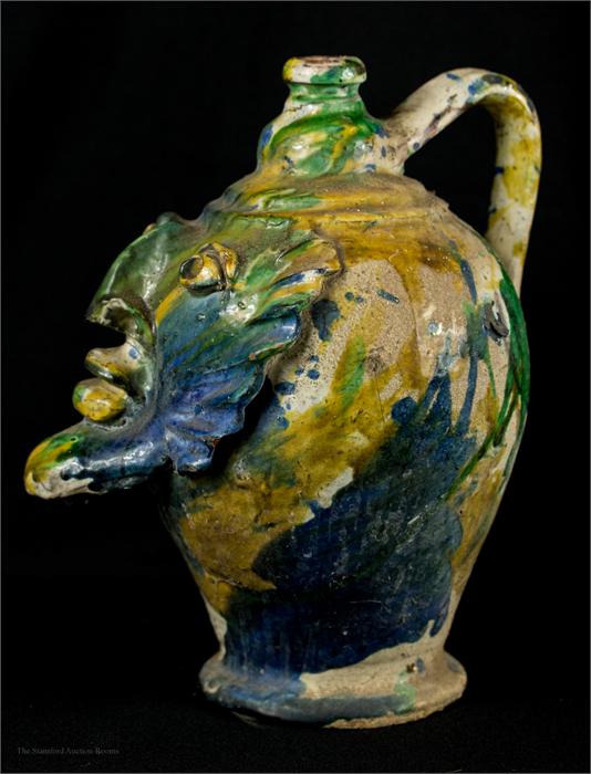 An early stoneware jar, yellow, green and blue slip glazed, modelled with a face mask.