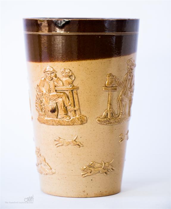 A Doulton Lambeth glazed stoneware jar/mug, embossed with figures drinking and hounds, impressed