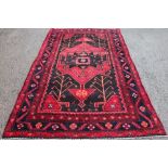 A Persian Lori wool carpet, worked with geometric flowers and motifs against a red and blue ground,