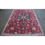 A Tabriz wool carpet, worked with a central motif and all over foliate design against a red ground,