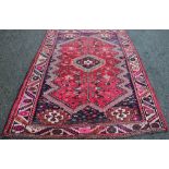 A Shiraz wool ground carpet, worked with a geometric design against a burnt red ground,