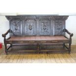 An 18th century carved oak settle, the four panel back decorated with armorial shields,