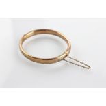 A 9ct yellow gold hinged bangle, the hollow bangle of plain form and with attached safety chain,