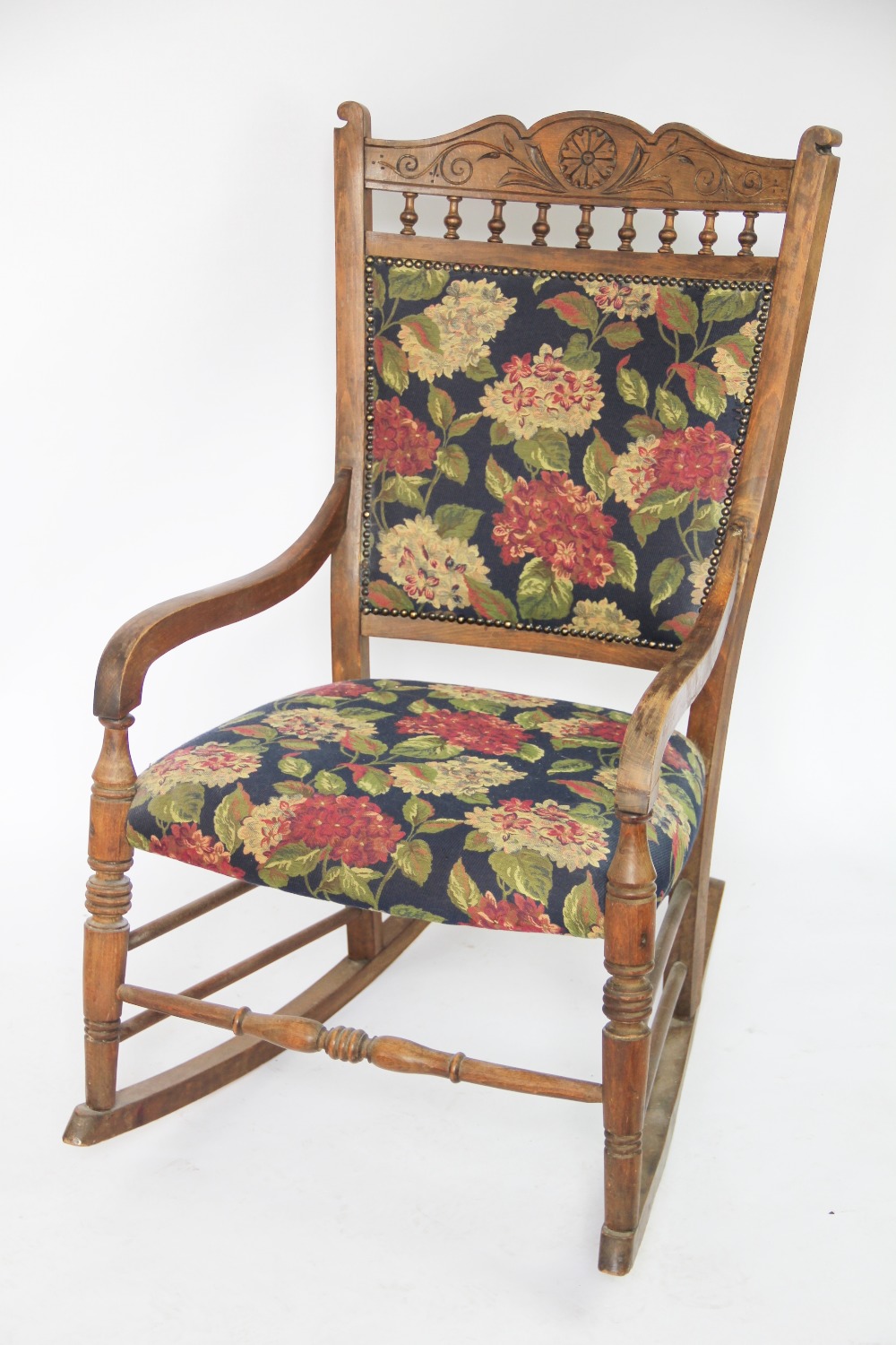 A late 19th century carved beech rocking chair, possibly American, with foliate floral upholstery,