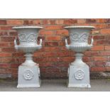 A pair of cast iron garden urns on stands, twin handled and decorated with flowers,