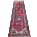 A Caucasian wool runner, worked with a foliate pattern against a red ground, 280cm x 73cm,