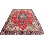 A hand woven wool carpet, worked with a central cartouche and floral detailing against a red ground,